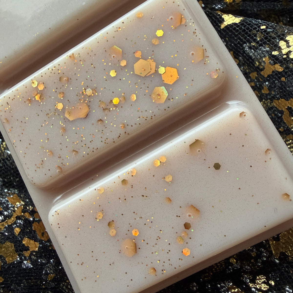 A close up of The Library bookish wax melts showing the smooth gold glitter front of the product soy wax bar