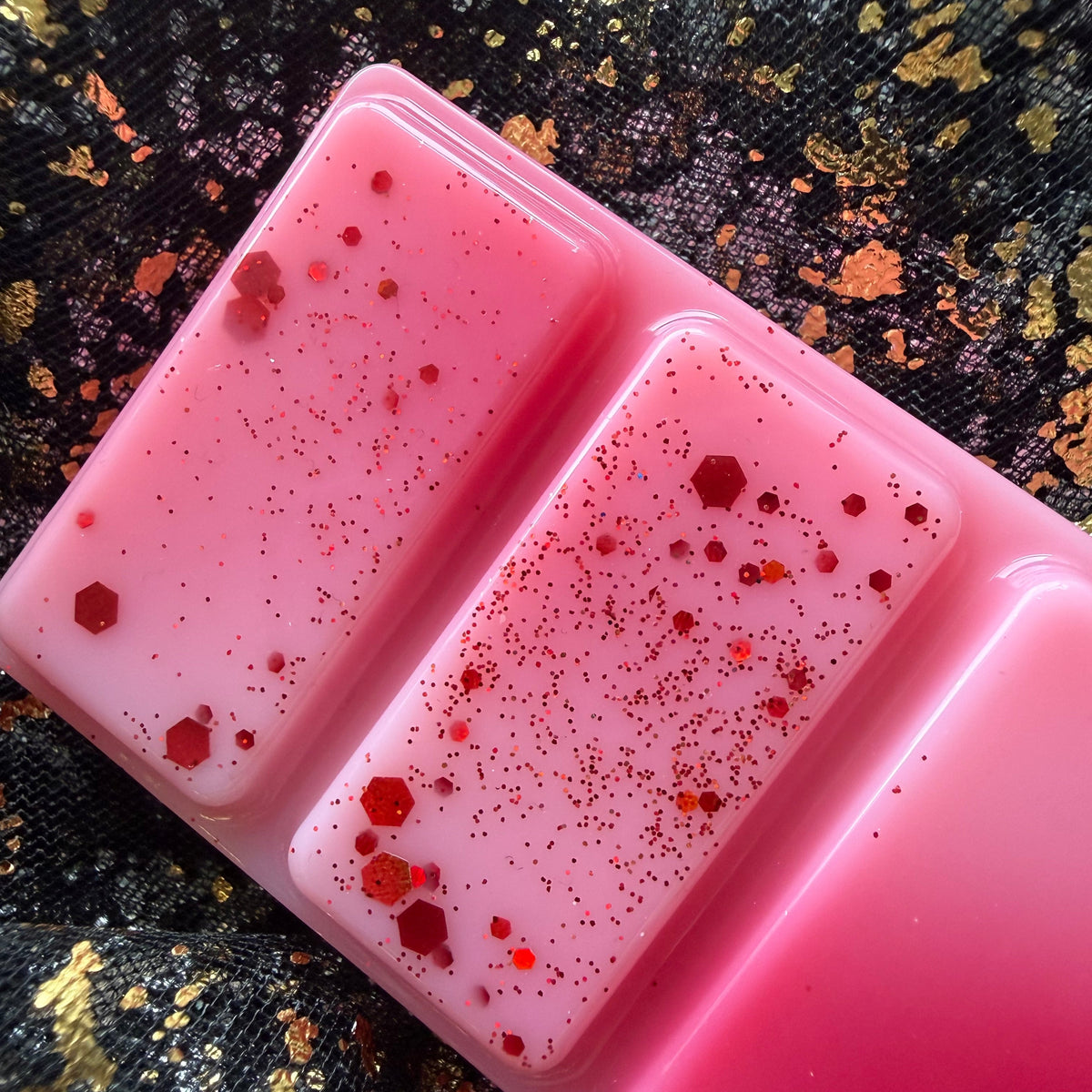 Close-up of the red and pink Fated Mates romantasy-inspired wax melt with red decorative detailing on black and gold fabric.