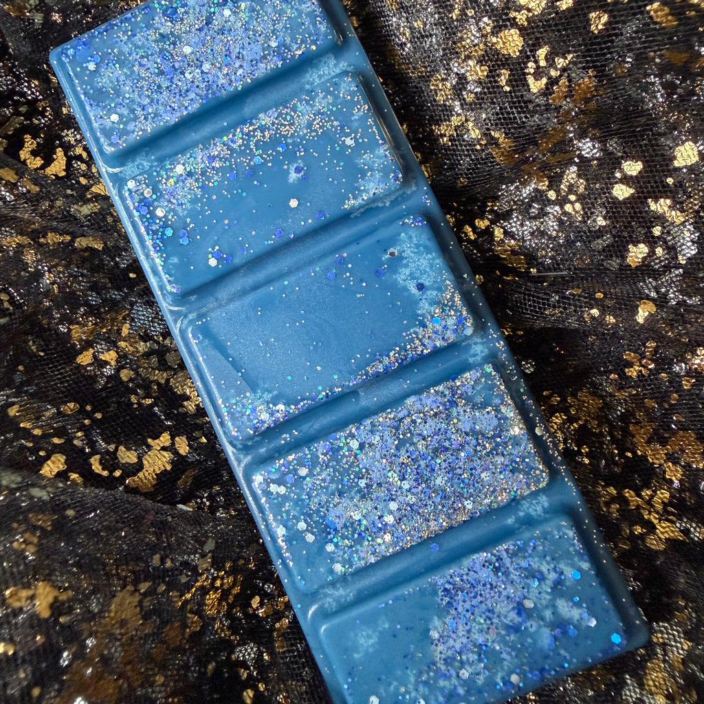 Deep blue Whitby Shadows wax bar displayed diagonally on black-and-gold fabric, with silver holographic glitter across all five segments.