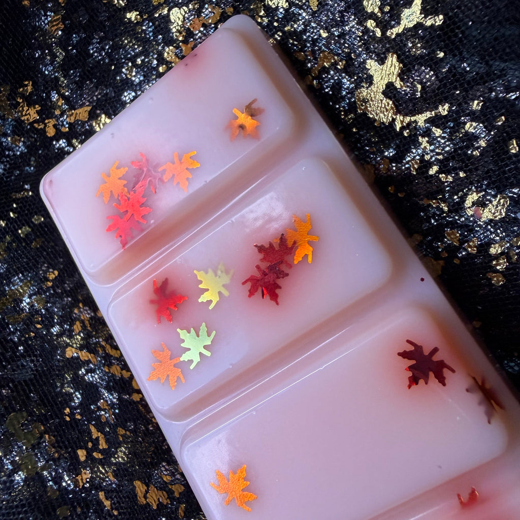 Close-up of Willa’s Apple Pie scented wax melt, showing small red, orange and yellow autumn-leaf glitter scattered across the pale pink peach coloured surface of a rectangular soy wax segment.
