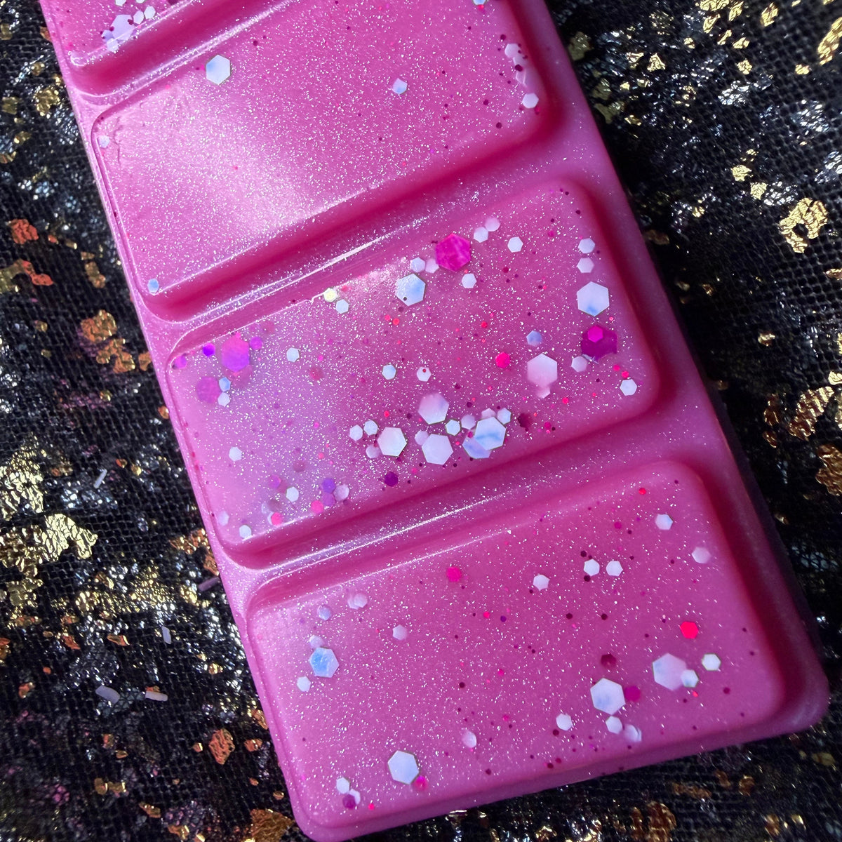 Close-up of the Winter Fairy Tale pink wax melt showing the sparkling pink and purple glitter scattered across the five hand poured soy wax segments.