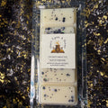 A clear plastic clamshell package containing four rectangular cream-colored wax melts with black speckles, featuring a white paper label that reads 'Once Upon A Sweet' and 'Coconutys About You'. The package is placed on a black sequined fabric background with gold glitter.