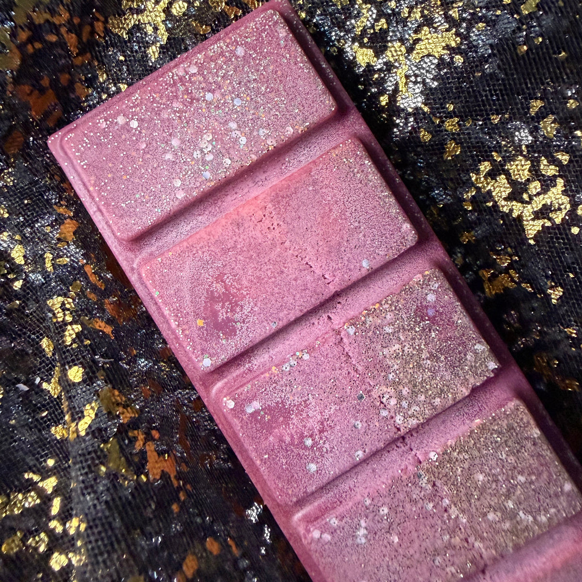 Close-up of the burgundy Cherry Bomb scented wax melt segments decorated with shimmering holographic glitter. Showing soy frosting on the discounted wax melt 